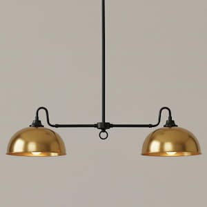 以下が含まれることがあります： 黒いフレームと2つの金色のドーム型シェードを備えた、2灯ペンダントライト。単一の垂直ロッドから吊り下げられ、湾曲したアームでシェードを支える水平バーがあります。