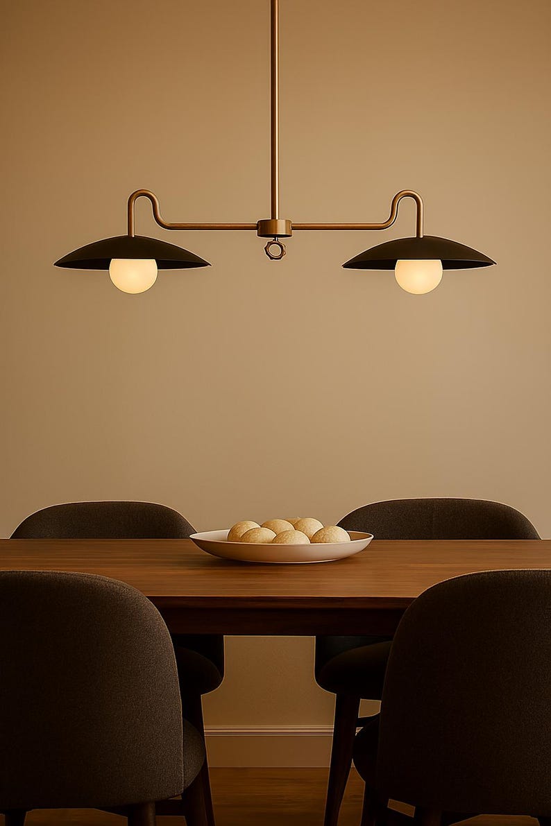 May include: A modern dining room scene featuring a dark wood table and four dark gray chairs. Above the table hangs a two-light pendant with black shades and spherical bulbs. A white bowl holds several round, golden-brown rolls.