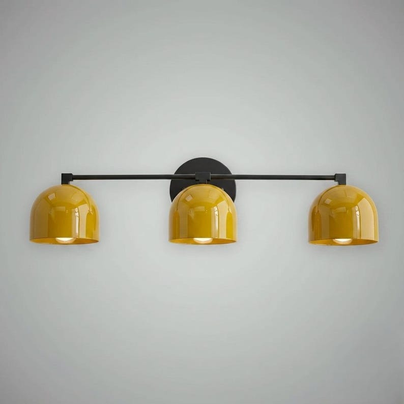 以下が含まれることがあります： 黒い金属フレームと円形の取り付けプレートを備えた、3灯の照明器具。この器具は、3つの黄色のドーム型のシェードを備えています。各シェードには電球が収められており、空間を照らします。デザインはモダンでミニマリストです。