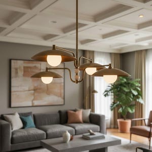 May include: A modern brass chandelier with four downward-facing, saucer-shaped shades, each housing a spherical light. The fixture hangs from a ceiling with a coffered design. The room features a gray sofa, artwork, and a large potted plant.