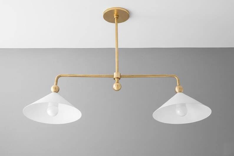 May include: A contemporary pendant light with two lights. The fixture features a gold-coloured metal frame and two white, cone-shaped shades. The light hangs from a ceiling mount, suitable for a kitchen or dining room.