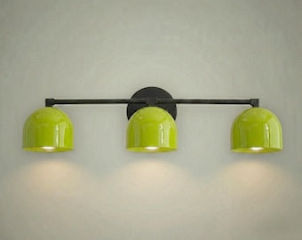 May include: A contemporary three-light fitting with a black metal frame and a circular mounting plate. It features three lime green dome-shaped shades. Each shade emits a warm light, ideal for a bathroom or vanity area.