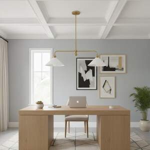 May include: A contemporary home office featuring a light wood desk, a beige chair, and a laptop. A gold-toned light fixture hangs above the desk. The walls are grey, and there are framed abstract art pieces. A potted plant sits in the corner.