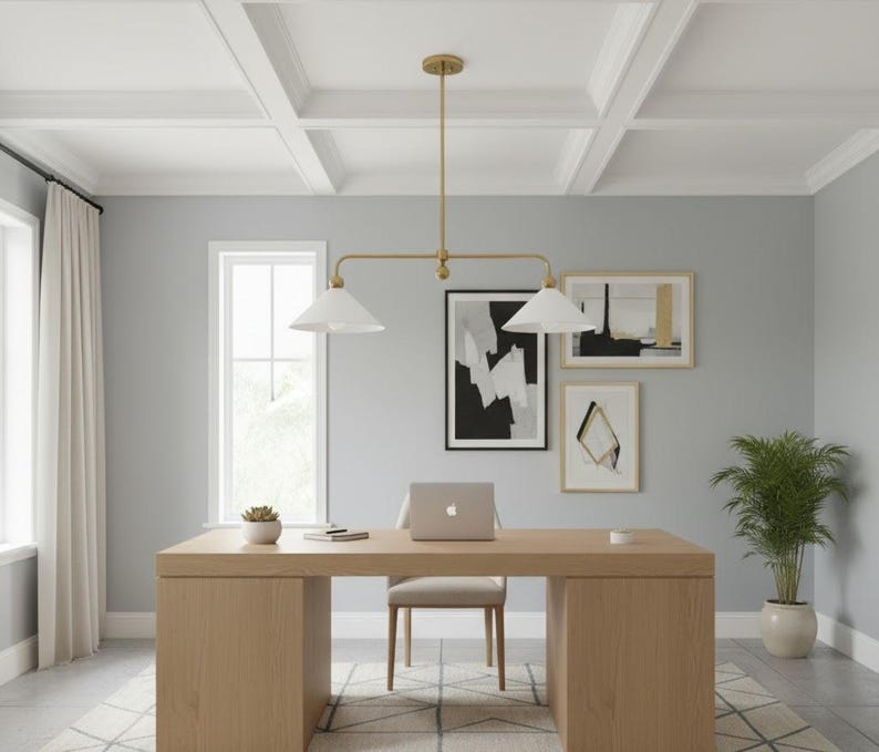 May include: A contemporary home office featuring a light wood desk, a beige chair, and a laptop. A gold-toned light fixture hangs above the desk. The walls are grey, and there are framed abstract art pieces. A potted plant sits in the corner.