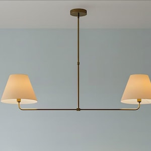 May include: A modern, two-light pendant lamp with a bronze finish. The lamp features two cream-colored, cone-shaped shades. The fixture is suspended from the ceiling by a central rod and horizontal arms.