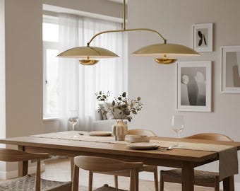 Könnte beinhalten: Ein Esszimmer mit einem Holztisch und Stühlen, gedeckt für eine Mahlzeit. Über dem Tisch hängt eine goldfarbene Pendelleuchte mit zwei Lichtern. Der Raum ist mit gerahmter Kunst und einer Vase mit Blumen dekoriert und schafft eine warme Atmosphäre.