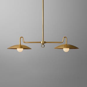 May include: A brass-colored, two-light pendant light fixture. The fixture has a central vertical rod with a horizontal bar extending to each side. Each side has a downward-facing, circular shade with a spherical light bulb.