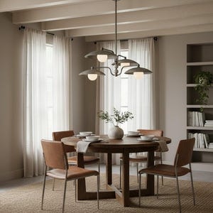 May include: A dining room set featuring a round wooden table, four brown leather chairs, and a metal chandelier with four lights. The room has neutral tones, sheer curtains, and a bookshelf.