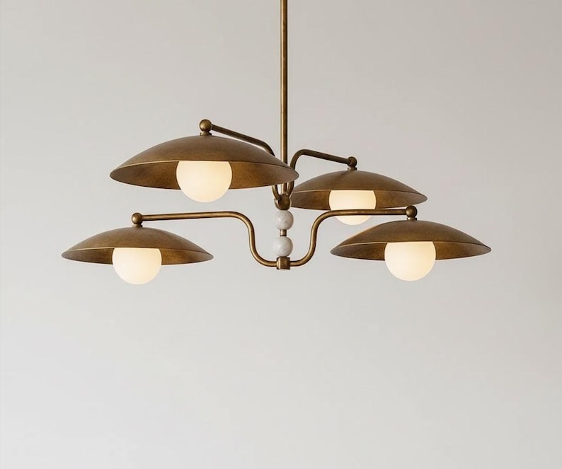 May include: A brass-toned chandelier with four lights. Each light has a round, white bulb and a curved, saucer-shaped shade. The fixture has a central stem and decorative white spheres.
