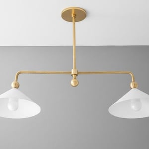May include: A contemporary pendant light with two lights. The fixture has a gold-coloured metal frame and two white, cone-shaped shades. It is designed to be mounted on a ceiling and is suitable for various interior styles.