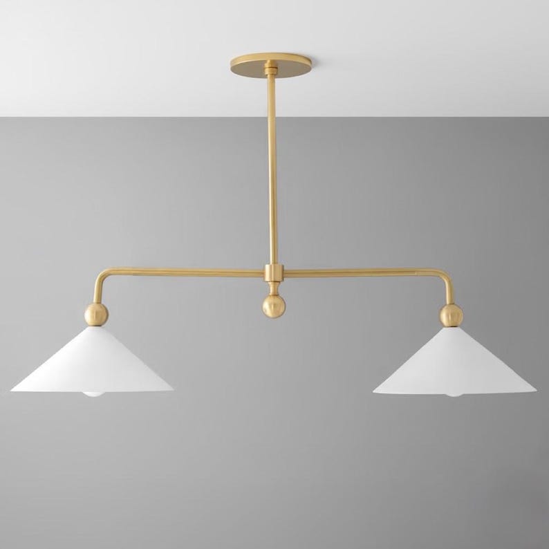 May include: A contemporary ceiling light fitting with a gold finish and two white, cone-shaped shades. The fixture features a horizontal bar with a light at each end and a central vertical support.