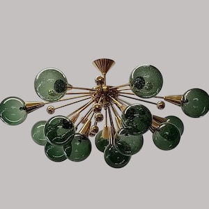 May include: A sputnik-style chandelier featuring a central gold-toned metal hub with multiple radiating arms. Each arm terminates in a spherical, translucent green glass globe with a textured, bubbly surface finish and a small internal light source.