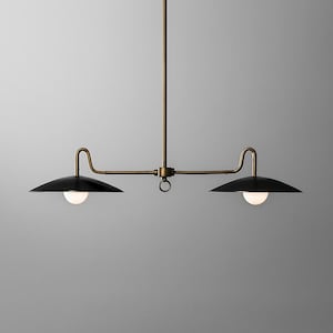 May include: A modern, two-light pendant light fixture. It features a brass-colored frame with two black, saucer-shaped shades. Each shade has a white, spherical light bulb. The fixture is suspended from the ceiling.