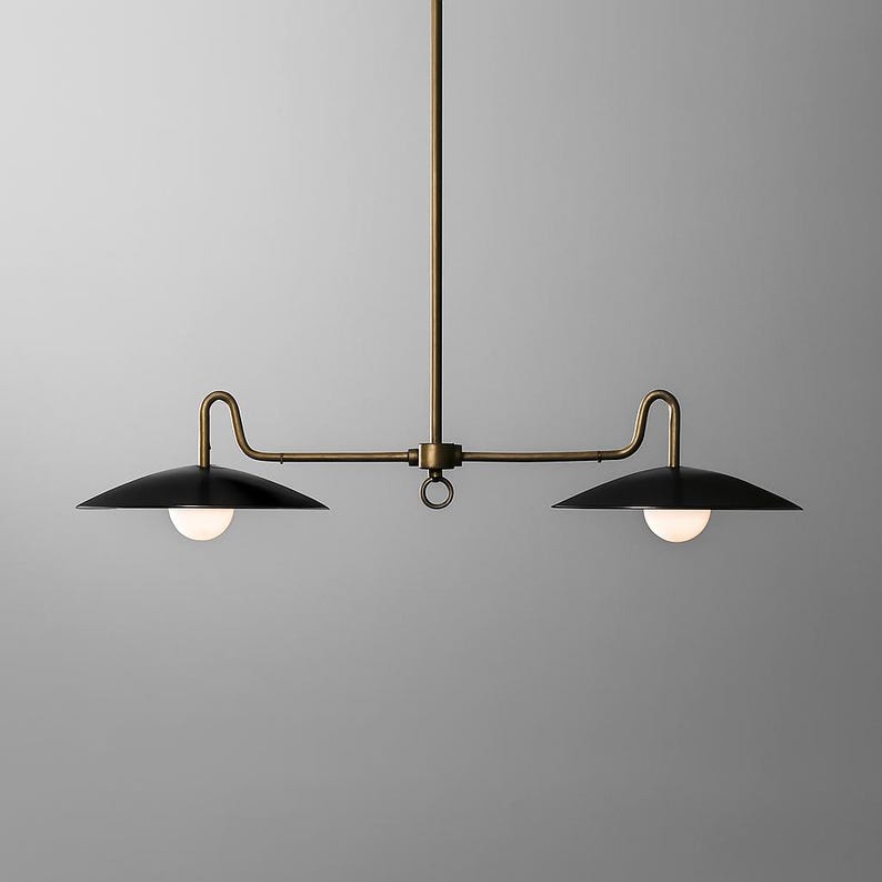 May include: A modern, two-light pendant light fixture. It features a brass-colored frame with two black, saucer-shaped shades. Each shade has a white, spherical light bulb. The fixture is suspended from the ceiling.