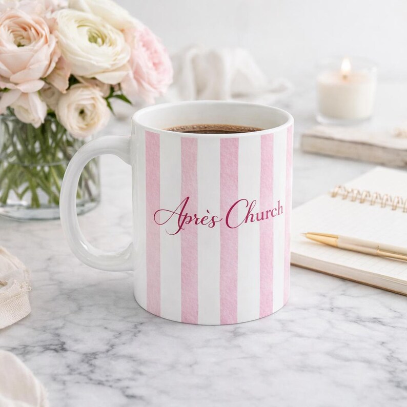 May include: White ceramic mug with pink vertical stripes and the text "Apr&egrave;s Church" in a cursive font. The mug is filled with a dark liquid and sits on a marble surface, next to a bouquet of flowers.