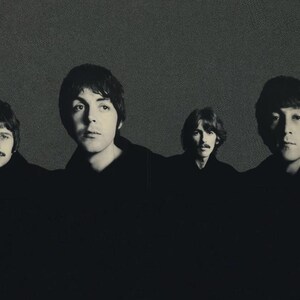 May include: Black and white photograph of four men, each with dark hair, looking forward. The image is a portrait, with the men's faces and upper bodies visible against a textured gray background. The men are wearing dark clothing.