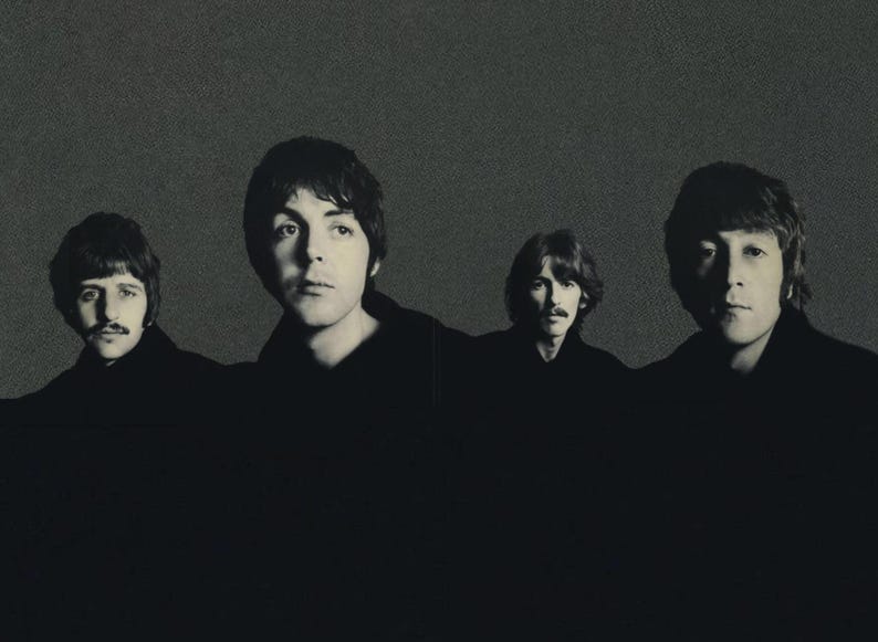 May include: Black and white photograph of four men, each with dark hair, looking forward. The image is a portrait, with the men's faces and upper bodies visible against a textured gray background. The men are wearing dark clothing.