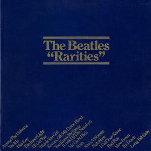 Puede incluir: Una portada de álbum azul oscuro con letras doradas. El título "The Beatles 'Rarities'" está centrado en la parte superior. Los títulos de las canciones, como "Across The Universe" y "Long Tall Sally", están en blanco en diagonal.