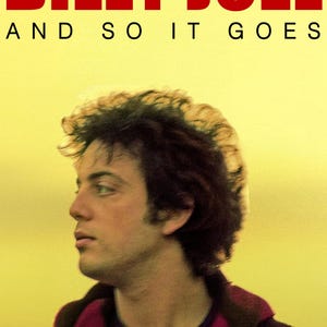 以下が含まれることがあります： 赤色の「BILLY JOEL」と黒色の「AND SO IT GOES」の文字が入ったDVDカバー。画像は、黄色の背景に、黒髪の男性の横顔が描かれています。DVDロゴは右下にあります。