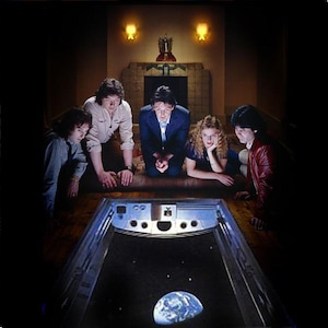 May include: A group of five people are gathered around a futuristic-looking display, gazing at a depiction of Earth in space. The scene is dimly lit, with a retro aesthetic. The display is a rectangular shape with a dark background.