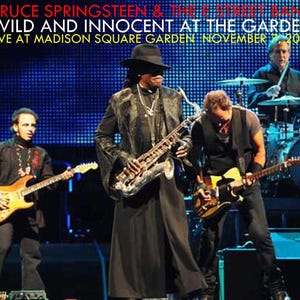 Może przedstawiać: Zdjęcie z koncertu na żywo Bruce'a Springsteena & The E Street Band. Scena jest oświetlona niebieskimi światłami. Członkowie zespołu grają na instrumentach, w tym na gitarach, saksofonie i perkusji. Tekst na zdjęciu brzmi: "Wild and Innocent at the Garden, Live at Madison Square Garden, November 7, 2009."