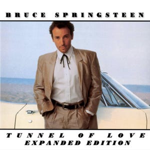 Puede incluir: Portada del álbum "Tunnel of Love Expanded Edition" de Bruce Springsteen. La imagen presenta a Springsteen con un traje color beige, camisa blanca y corbata negra, apoyado en un coche antiguo. El título del álbum y el nombre del artista se muestran en negrita, en negro.