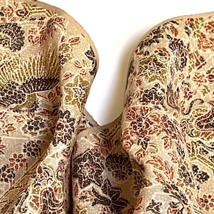 Puede incluir: Primer plano de una tela beige con un detallado estampado floral en tonos marrones, verdes y rojos. La tela tiene un aspecto texturizado y un fondo suave y neutro. El diseño presenta intrincados elementos botánicos.