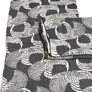 May include: Black fabric with a white crane pattern. The fabric is folded in thirds.