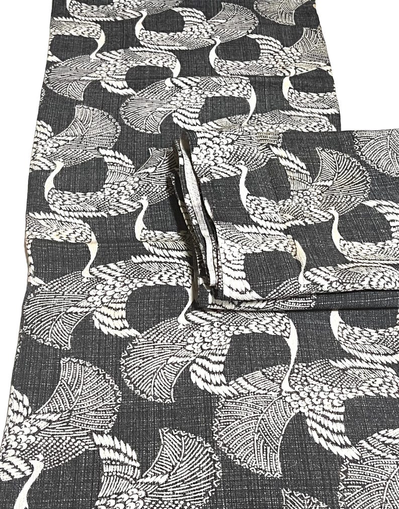 May include: Black fabric with a white crane pattern. The fabric is folded in thirds.