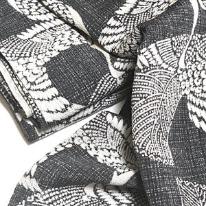 May include: Black and white fabric with a repeating pattern of stylized birds and leaves. The fabric is folded and textured.
