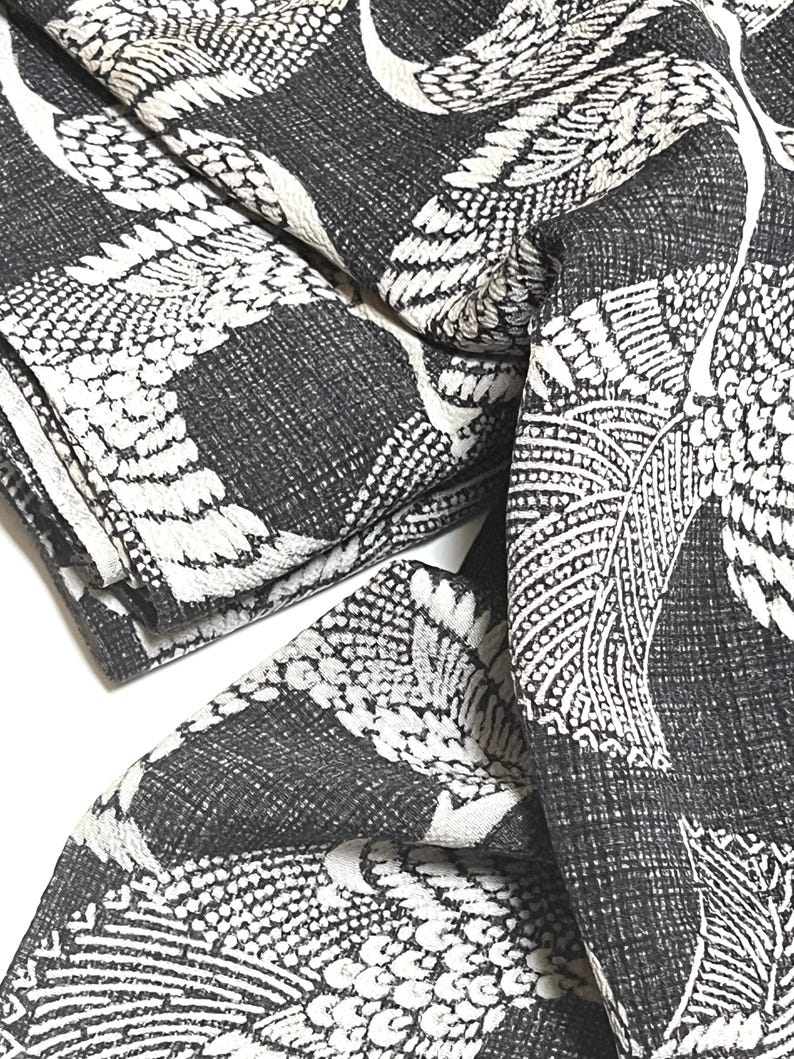 May include: Black and white fabric with a repeating pattern of stylized birds and leaves. The fabric is folded and textured.