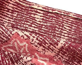 May include: Close-up of a burgundy fabric with a white and pink abstract pattern. The fabric has a textured, slightly shimmery surface.
