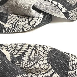 May include: Black and white fabric with a repeating pattern of stylized crane wings. The fabric has a textured, woven look.