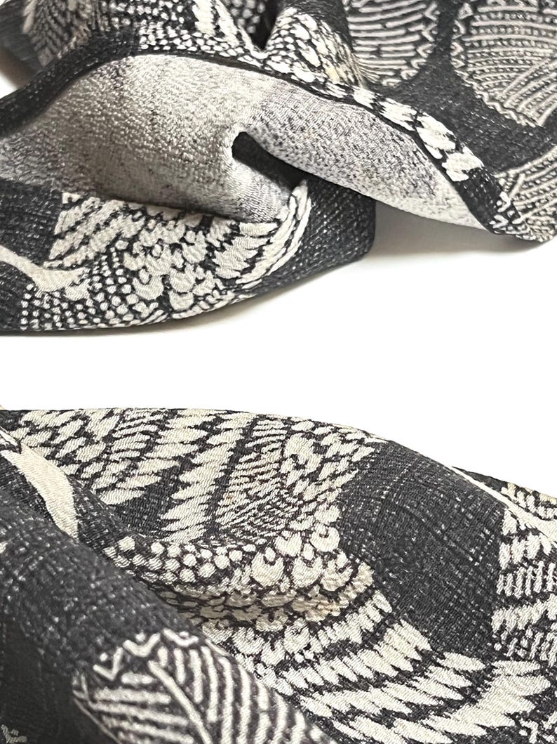 May include: Black and white fabric with a repeating pattern of stylized crane wings. The fabric has a textured, woven look.