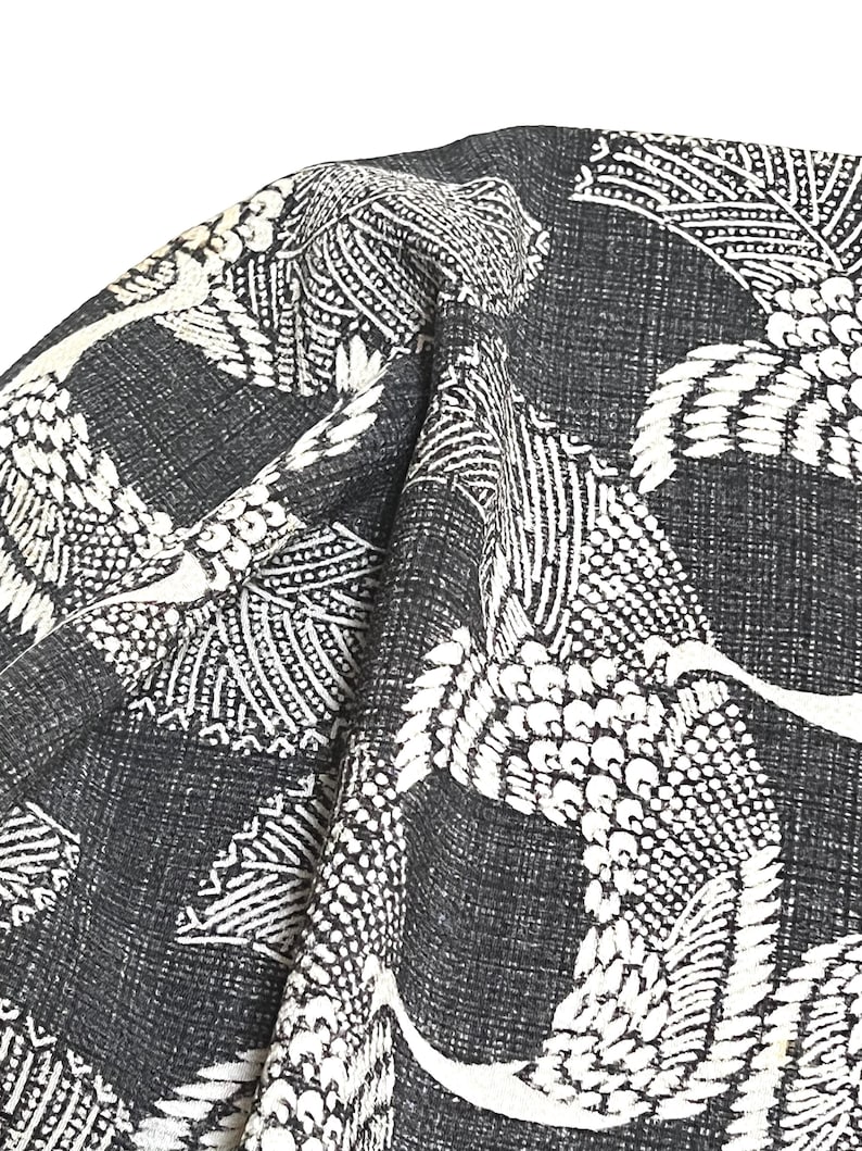 May include: Black fabric with a white crane pattern. The fabric has a textured woven look.