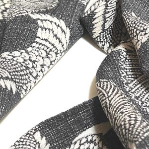 May include: A black and white patterned scarf with a repeating design of stylized birds. The scarf is made of a soft, woven fabric.