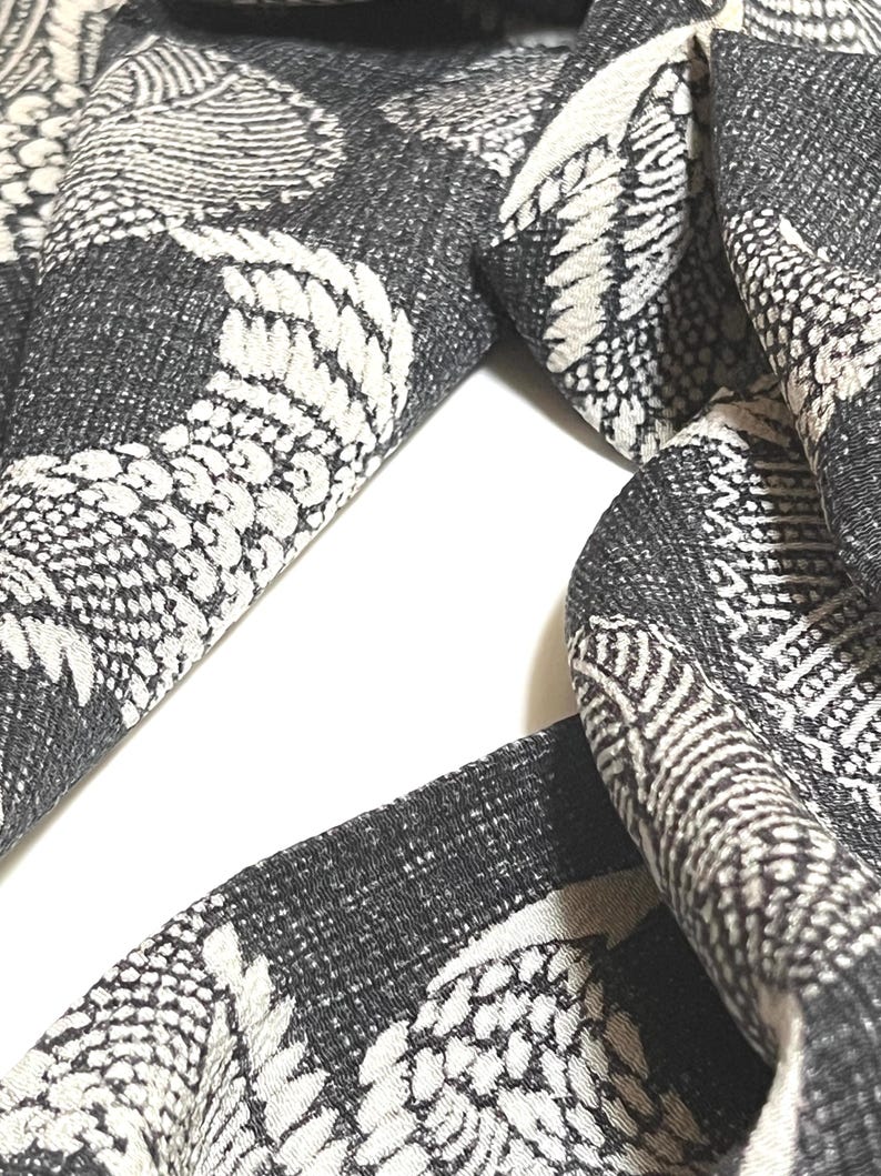 May include: A black and white patterned scarf with a repeating design of stylized birds. The scarf is made of a soft, woven fabric.