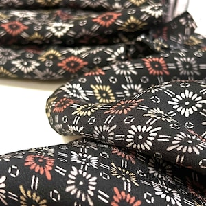 May include: Black fabric with a repeating pattern of white, pink, and gold stylized flowers. The fabric is folded and textured.