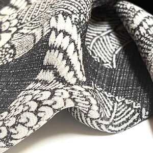 May include: Black and white patterned fabric with a textured surface. The fabric is folded and draped, showing the intricate design.