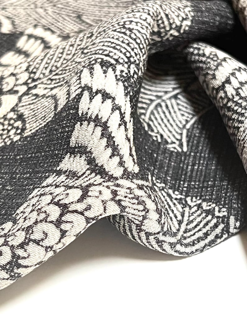 May include: Black and white patterned fabric with a textured surface. The fabric is folded and draped, showing the intricate design.