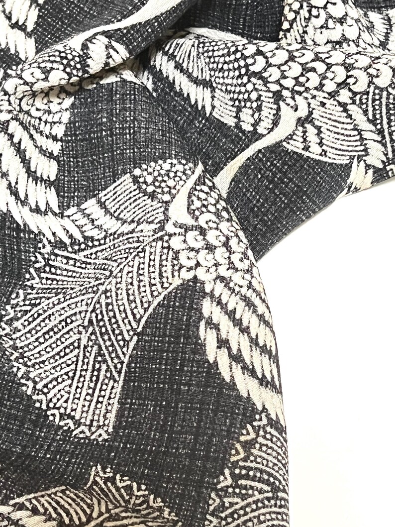 May include: Black fabric with a white crane pattern. The fabric is textured and has a subtle sheen. The cranes are stylized and have intricate details.