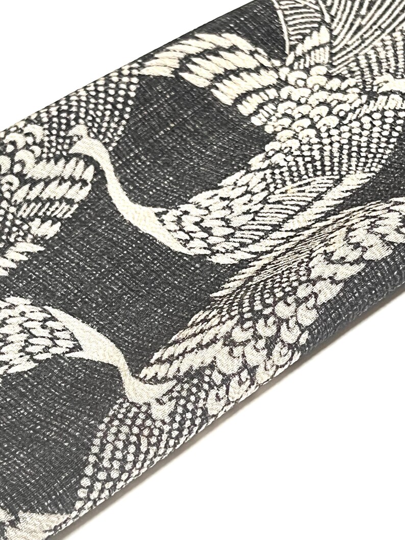 May include: Black fabric with a white crane pattern. The fabric is folded in half and the crane pattern is visible on both sides.