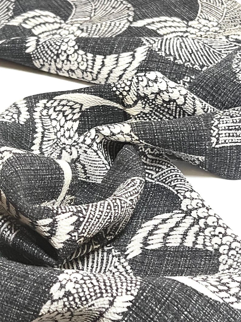 May include: Black and white fabric with a repeating pattern of stylized birds. The fabric has a textured surface.