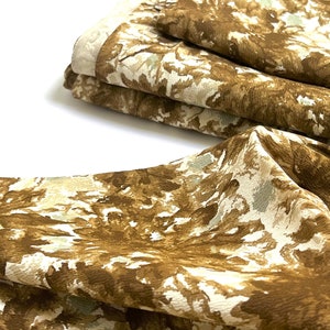 May include: Brown and white patterned fabric with a floral design. The fabric is folded in a stack.