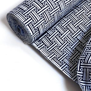 May include: A roll of white fabric with a black geometric pattern. The fabric has a woven look and is ideal for quilting, crafts, or home decor.