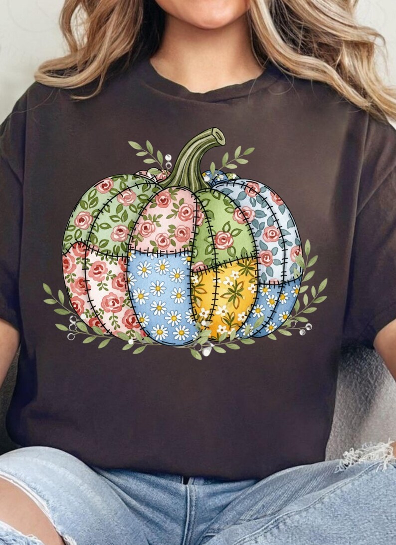 K&ouml;nnte beinhalten: Dunkelbraunes T-Shirt mit einem Patchwork-K&uuml;rbis-Design. Der K&uuml;rbis besteht aus floralen Mustern in Rosa, Gr&uuml;n, Blau und Gelb, mit einem gr&uuml;nen Stiel und Bl&auml;ttern. Das Design ist auf dem T-Shirt zentriert.