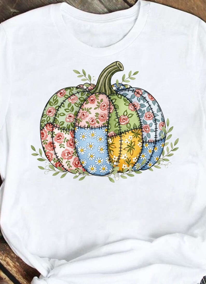 K&ouml;nnte beinhalten: Wei&szlig;es T-Shirt mit einem Patchwork-K&uuml;rbis-Design. Der K&uuml;rbis ist in Abschnitte mit Blumen- und G&auml;nsebl&uuml;mchenmustern in Rosa, Blau, Gr&uuml;n und Gelb unterteilt. Gr&uuml;ne Bl&auml;tter und ein Stiel vervollst&auml;ndigen das Design.