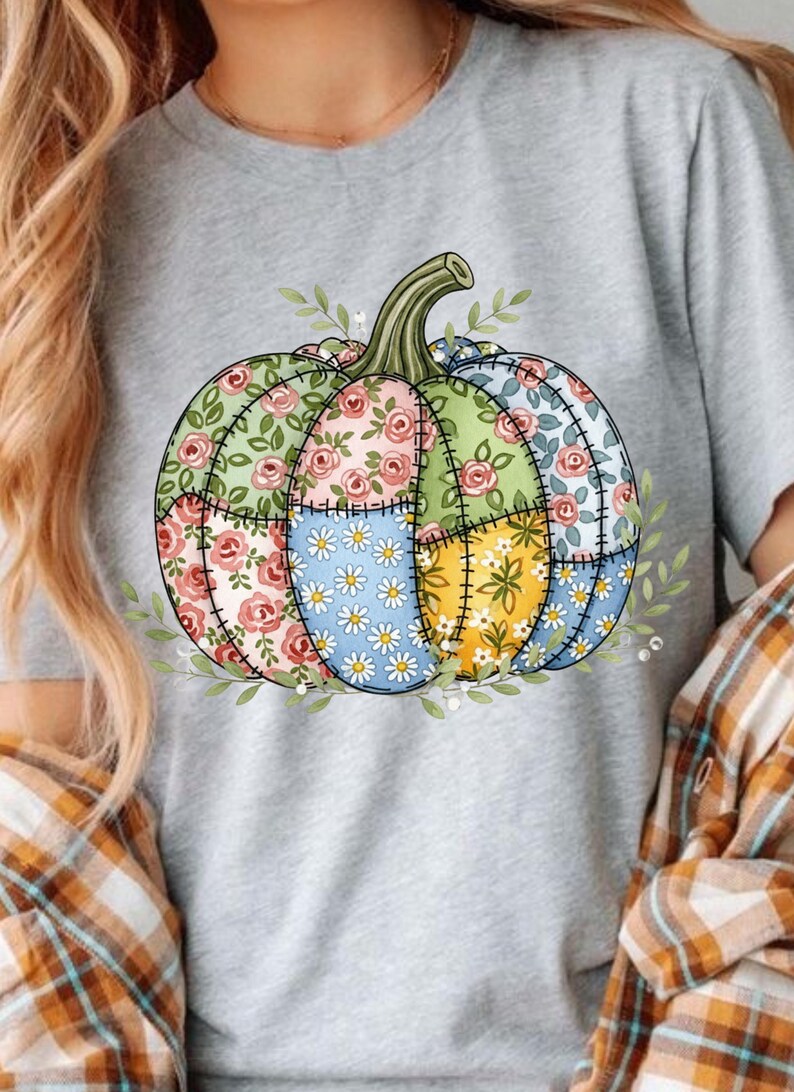 K&ouml;nnte beinhalten: Graues T-Shirt mit einem bunten K&uuml;rbisdesign. Der K&uuml;rbis ist in Abschnitte mit floralen Mustern in Rosa, Gr&uuml;n, Blau und Gelb unterteilt. Gr&uuml;ne Bl&auml;tter und ein Stiel vervollst&auml;ndigen das Design.