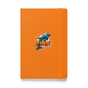 May include: A bright orange hardcover notebook with a vertical elastic closure band. The front cover features a central graphic of a teal dolphin wearing a white helmet, positioned over the orange text FINS TV with a white sunburst background.