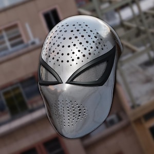 May include: A metallic silver full-face mask featuring a smooth, reflective surface with a pattern of small circular perforations across the forehead and mouth area. The mask includes two large, almond-shaped eye openings with black borders.